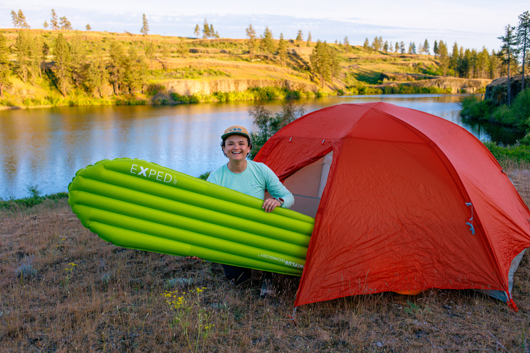 holding a lime green exped leeping pad and sitting in a red Big Agnes tent